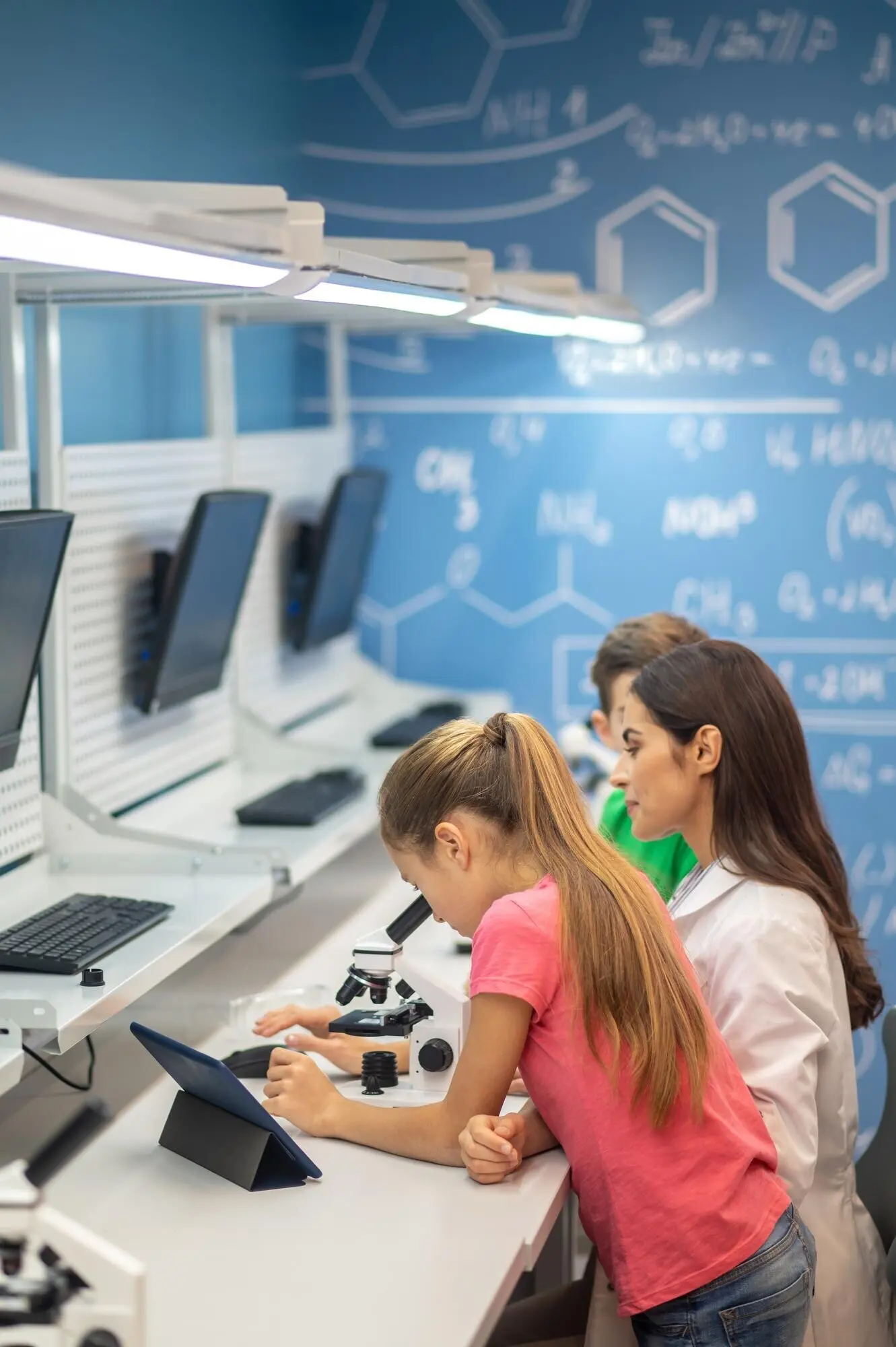 Mädchen in der Nähe eines Mikroskops und beobachtende Lehrkraft